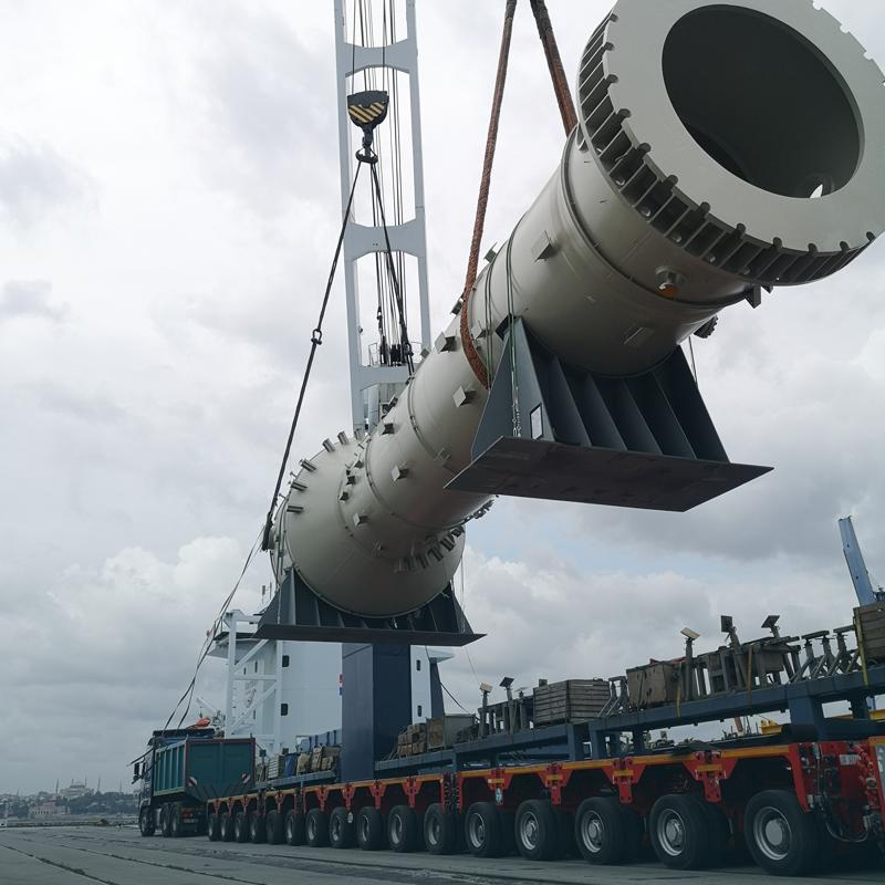 Port crane lifting a large cylindrical vessel.